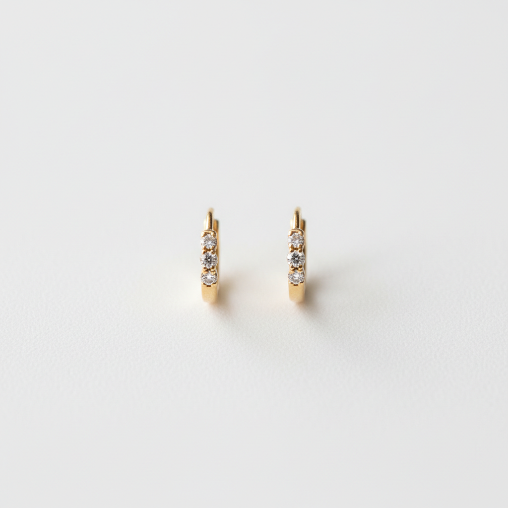 Flat lay of 14K yellow gold diamond huggie hoop earrings on white surface