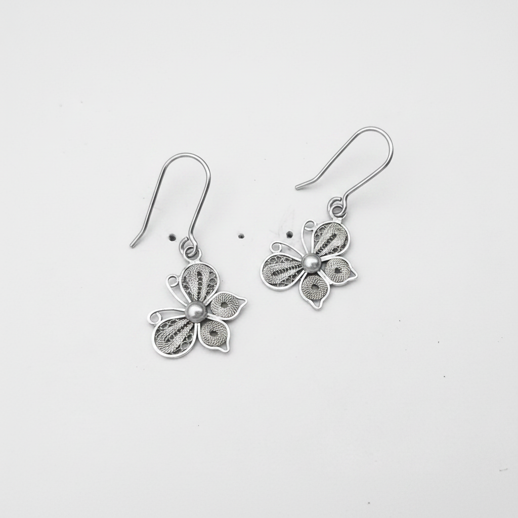 Sterling silver filigree butterfly drop earrings suspended sideways on white background, professional jewelry photography