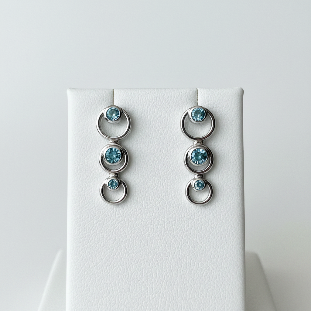 14kt white gold graduated circle drop earrings with three bezel-set blue topaz stones on white background