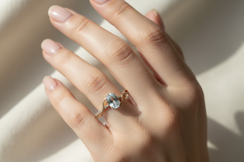 Model wearing 10K yellow gold oval aquamarine ring with diamond swirl accent, stone pointing down