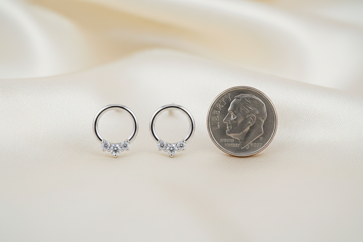 14K white gold three-diamond open circle stud earrings standing upright next to a dime showing true petite scale