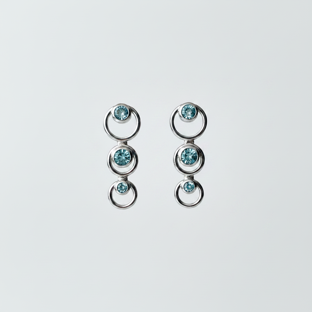 14kt white gold graduated circle drop earrings with three bezel-set blue topaz stones, suspended on bright white background