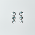 14kt white gold graduated circle drop earrings with three bezel-set blue topaz stones, suspended on bright white background