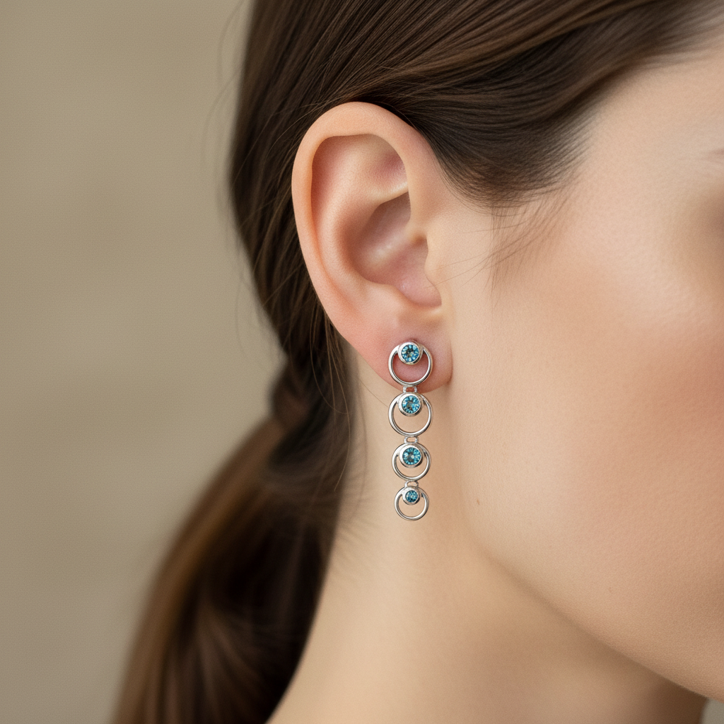 14kt white gold graduated circle drop earrings with three bezel-set blue topaz stones worn on model's ear, lifestyle shot